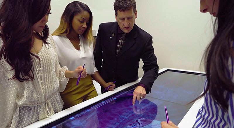 Three adults sit around a table with a laptop on it.